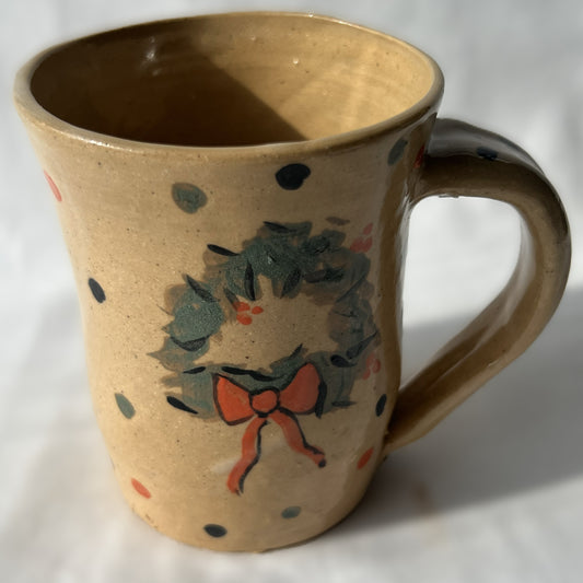 Ceramic mug with wreath design on a tan background