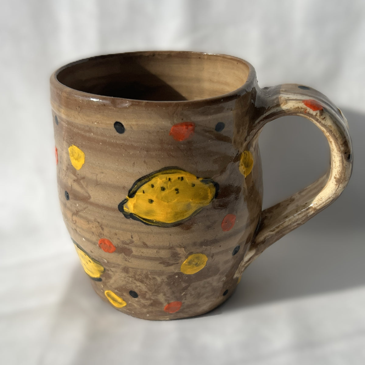 Brown ceramic mug with yellow lemon designs on a white background