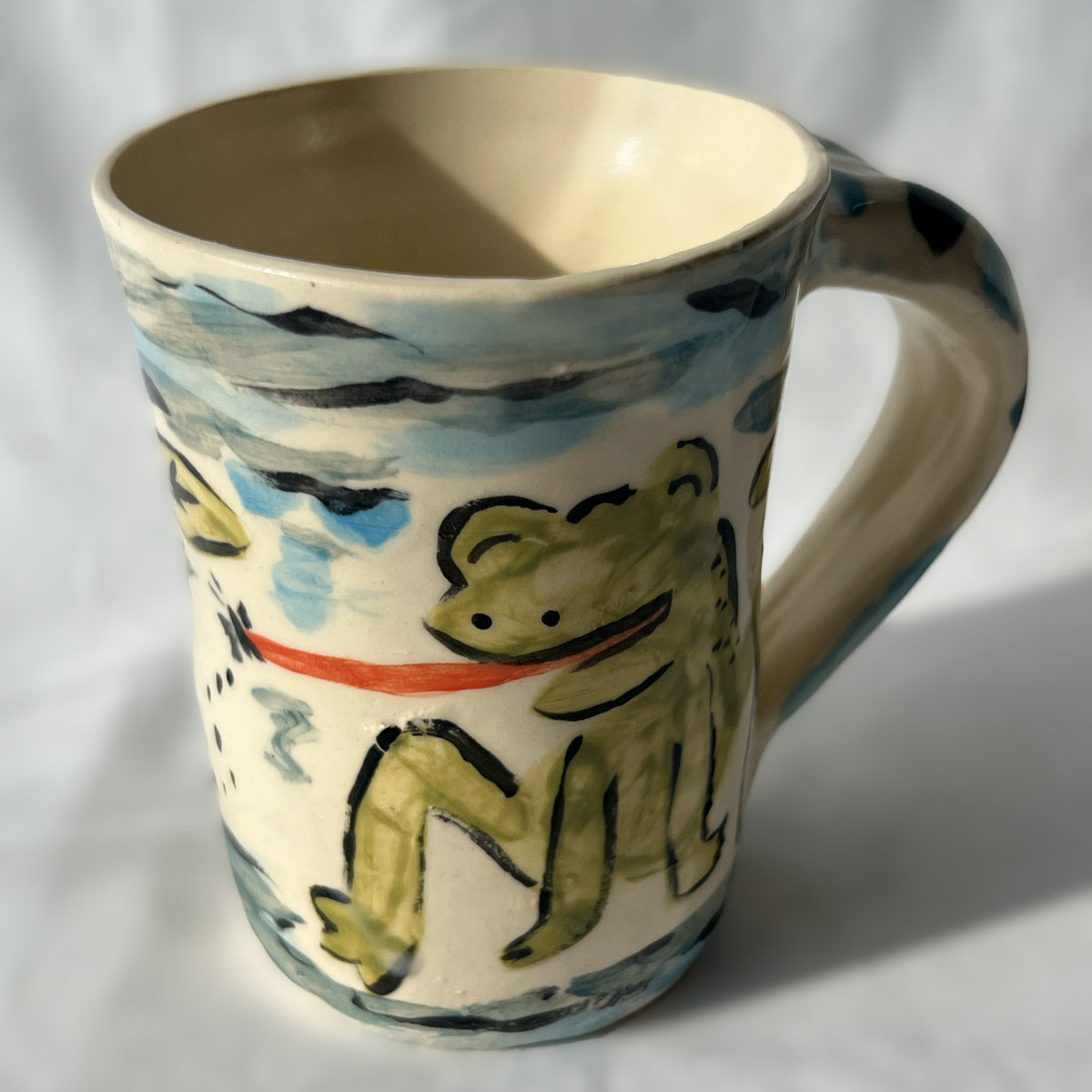 Ceramic mug with a painted frog design on a white background