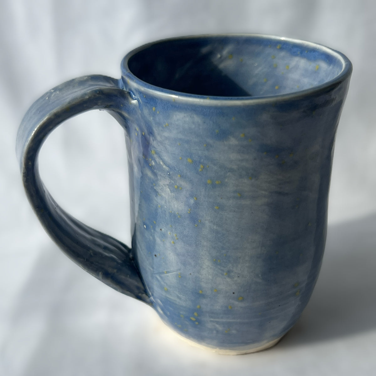 Blue ceramic mug with star-like speckles on a white background with smooth surface