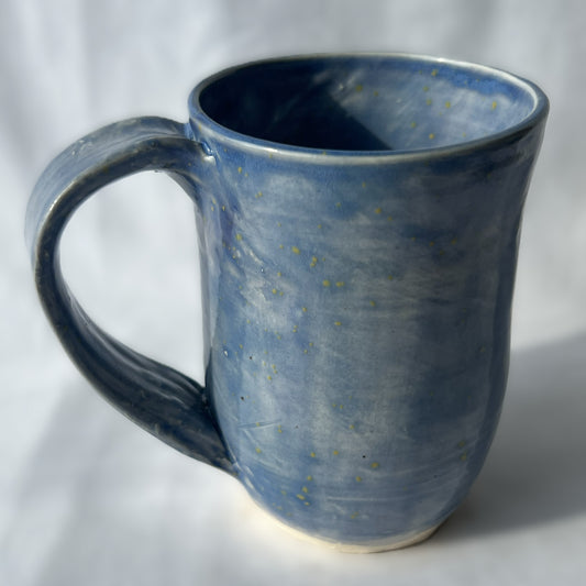 Blue ceramic mug with star-like speckles on a white background with smooth surface