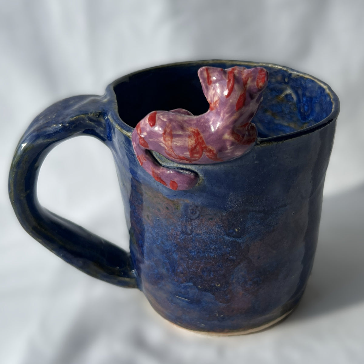 Blue ceramic mug with a purple and red cat figurine on the rim