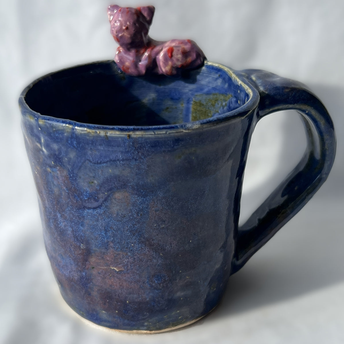 Blue ceramic mug with a purple and red cat figurine on the rim