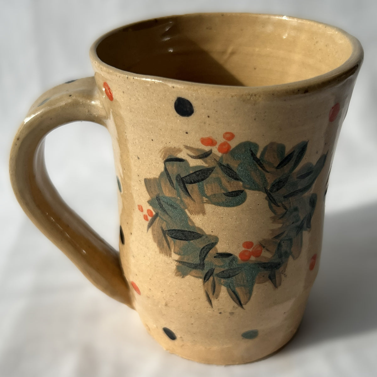 Ceramic mug with wreath design on a tan background