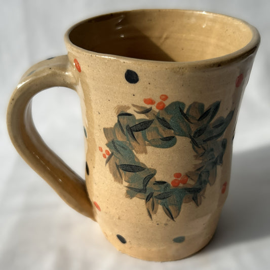Ceramic mug with wreath design on a tan background