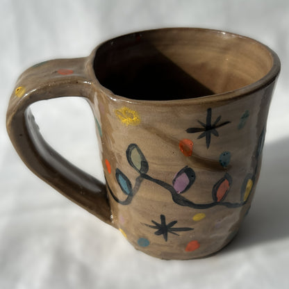 Ceramic mug with colorful Christmas light strand designs on a brown background