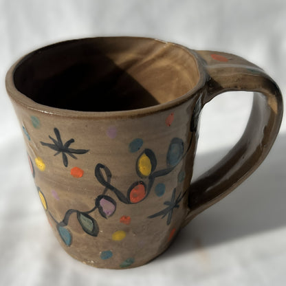 Ceramic mug with colorful Christmas light strand designs on a brown background