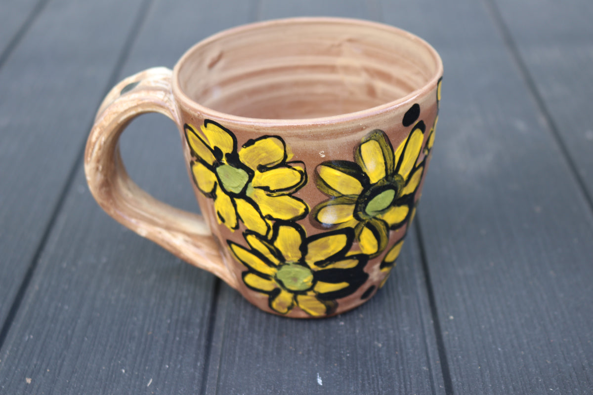 Ceramic mug with yellow floral design on a dark wooden surface