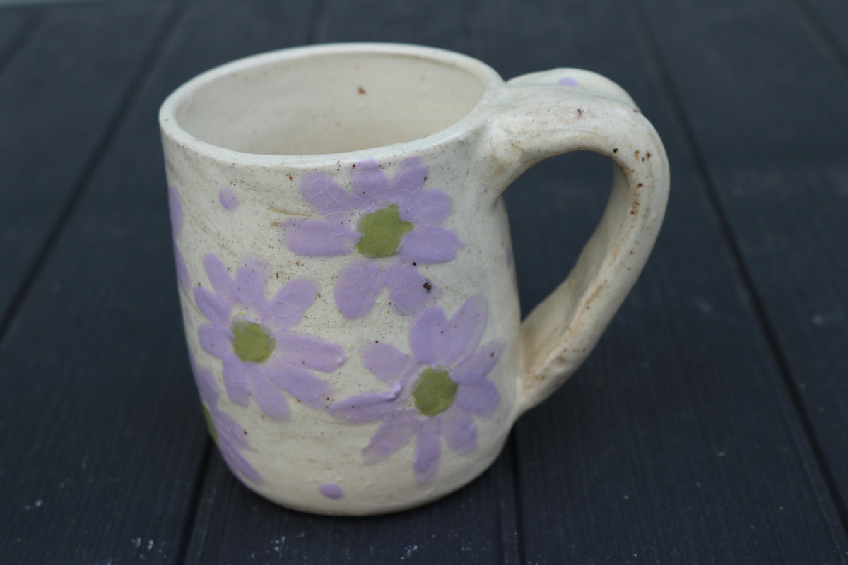 Ceramic mug with purple floral patterns on a dark wooden surface
